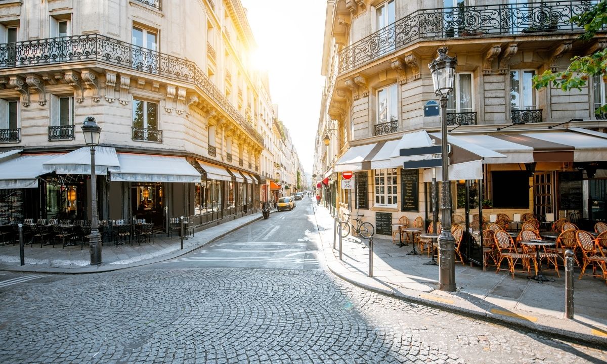 A photo of a Parisian street with two cafes on either side and a cobblestone street that splits the middle.