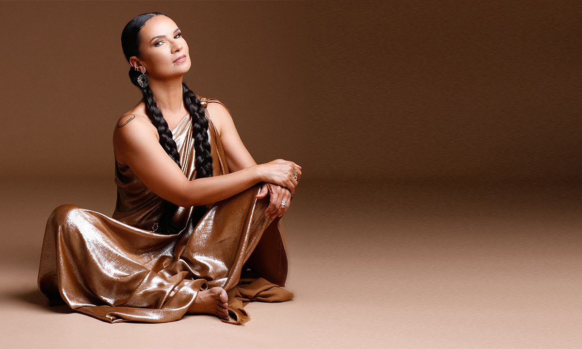 Ohm Dialddar sitting cross legged in a brown silk dress with her hair in two braids and arms crossed onto her knee smiling slightly at the camera